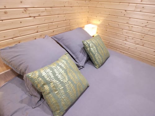 Cozy bedroom at Ilot Cosy and Spa with purple bedding, decorative cushions, and wooden ceiling lighting