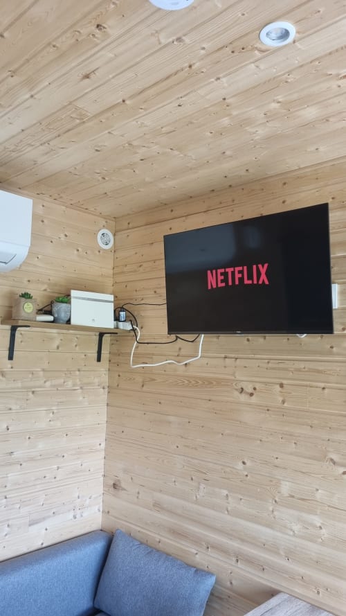 Cozy wooden cabin interior with Netflix on TV, shelf, and seating at Ilot Cosy and Spa