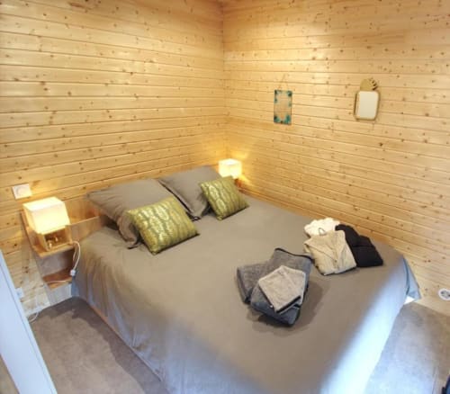 Cozy wooden bedroom at Ilot Cosy and Spa with bed, green pillows, warm lighting, and folded linens