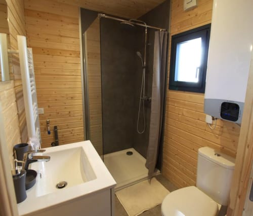 Modern wooden bathroom with walk-in shower, white sink, toilet, and window at Ilot Cosy and Spa, Luçay-le-Mâle