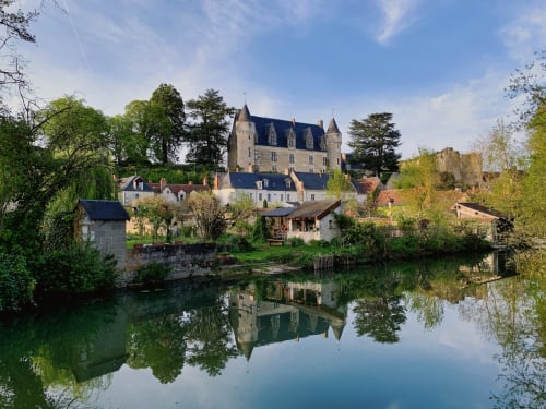 Château de Luçay-le-Mâle reflected in calm water, surrounded by lush greenery and historic buildings in France.