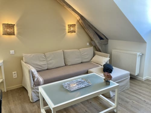 Petit salon cosy sous les toits à La Maison Virginie avec canapé beige, table basse blanche et vue sur Montargis