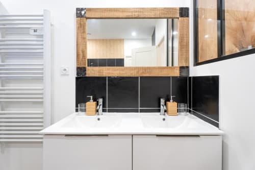 Modern bathroom vanity with dual sinks, black tile backsplash, wooden mirror frame at Wellkhome Bordeaux apartment