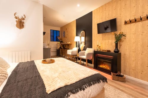 Cozy Bordeaux apartment bedroom with wooden walls, fireplace, bed, seating area, and flat-screen TV