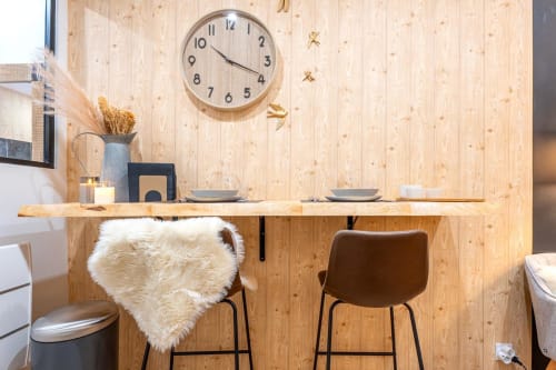Modern studio apartment workspace in Bordeaux with wooden wall, desk, bar seating, wall clock, and dining area at Wellkhome