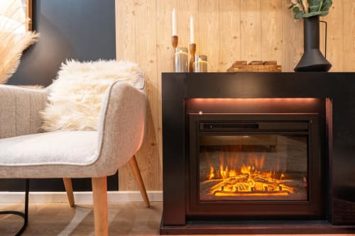 Modern living room at Wellkhome Bordeaux with fireplace, beige armchair, wooden walls, and candlesticks on mantel