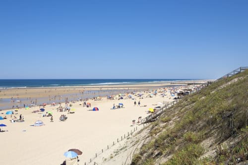 Plage de sable bondée à Mimizan avec parasols, baigneurs et dunes côtières avec escaliers d'accès