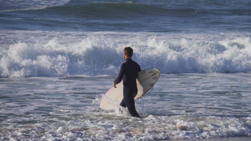 Surfeur en combinaison entrant dans les vagues de la plage de Mimizan, France près des Logis d'Argent
