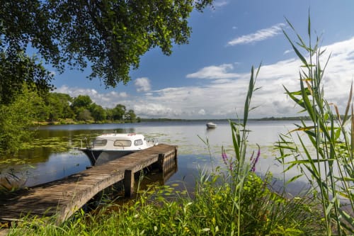 Ponton en bois avec bateaux amarrés sur le lac calme à Les Logis d'Argent, Mimizan, entouré de verdure luxuriante
