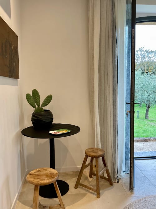 Modern room corner at Provence Km28 with cactus plant on black table, wooden stools, and garden view through open glass