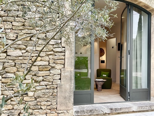 Garden view terrace entrance at Provence Km28 in Gordes with olive tree, stone walls, and modern glass doors to Les Oliviers
