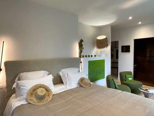 Modern bedroom at Provence Km28 in Gordes with beige linens, straw hats, green accent chair, and garden view artwork