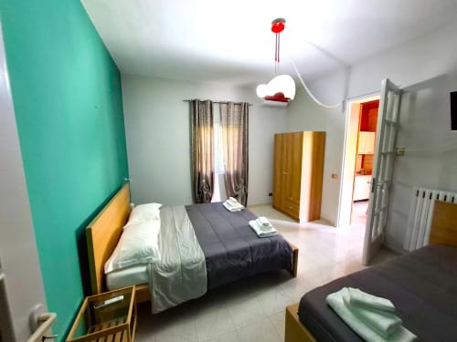 Camera da letto moderna a Newhouse Bari con parete azzurra, letti matrimoniali, arredamento in legno e bagno ensuite.