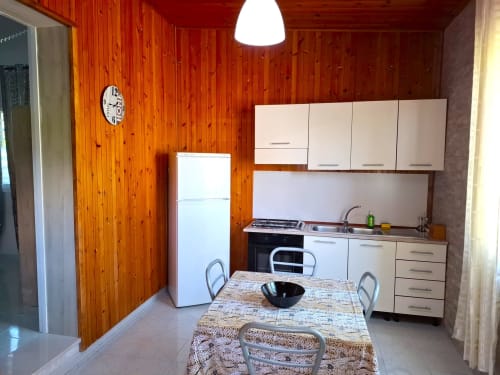 Zona cucina-soggiorno moderna dell'appartamento Newhouse a Bari con pareti in legno, armadi bianchi e tavolo da pranzo