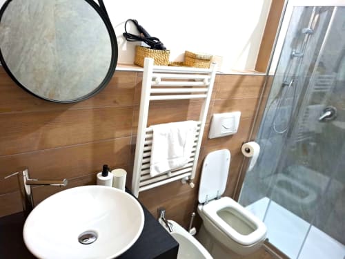 Bagno moderno all'appartamento Newhouse di Bari con specchio rotondo, wc bianco, scaldasalviette e box doccia