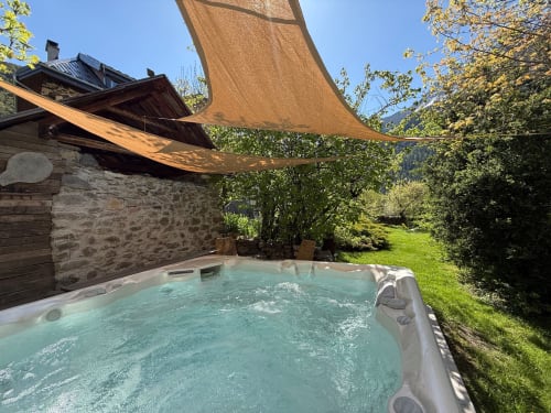 Bain à remous sous voile d'ombrage à Les Méans B&B à Méolans-Revel, avec bâtiment en pierre et paysage alpin