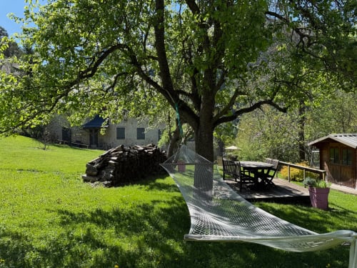Espace de détente ombragé aux Méans B&B à Méolans-Revel avec tables, bancs et chaumière en pierre