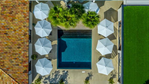 Vue aérienne de la cour piscine La Maison D'ambrine avec parasols blancs, palmiers et eau turquoise à Chamaret, France.