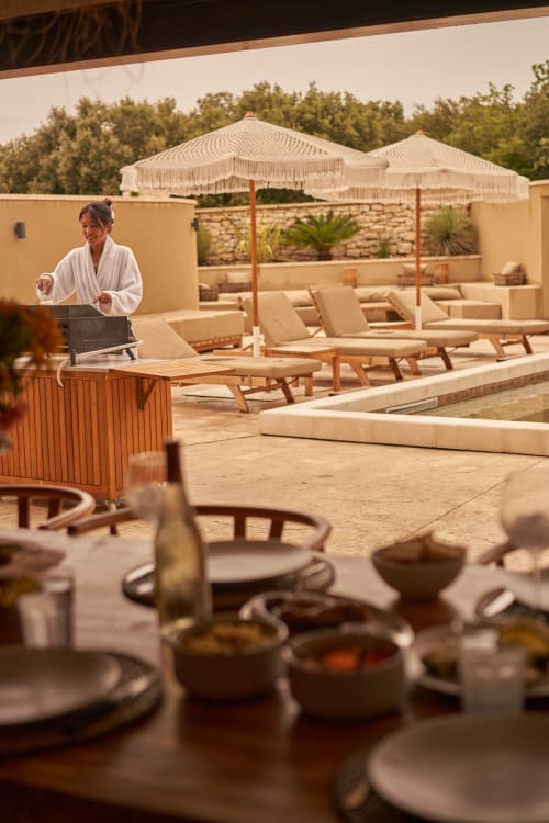Mujer en la terraza de la piscina del hotel boutique La Maison D'ambrine en Chamaret, Francia, con sombrillas y tumbonas
