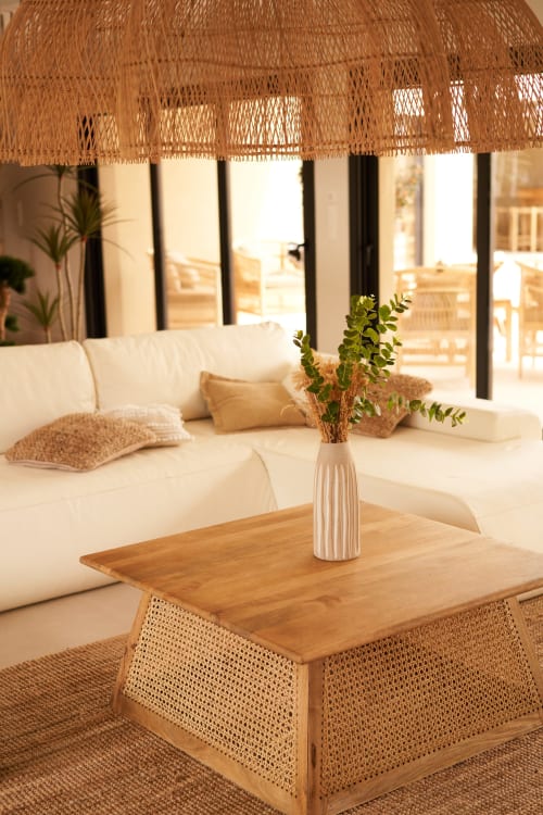 Elegante sala de estar en La Maison D'ambrine con sofá color crema, mesa de café de madera, acentos de ratán tejido y luz natural