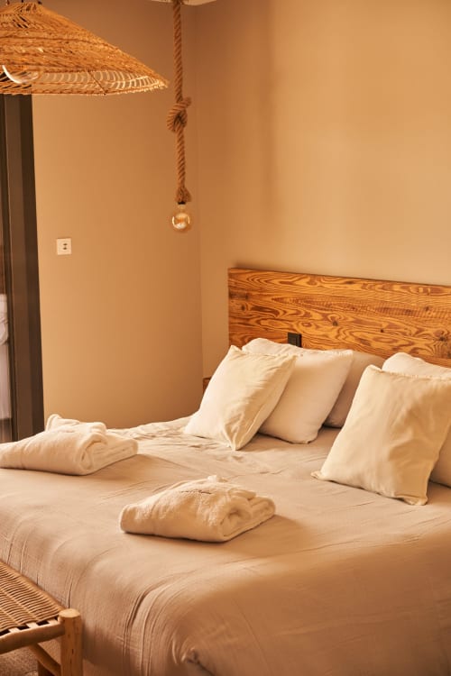 Acogedora habitación de villa con cabecera de madera, almohadas crema y lámpara colgante tejida en La Maison D'ambrine