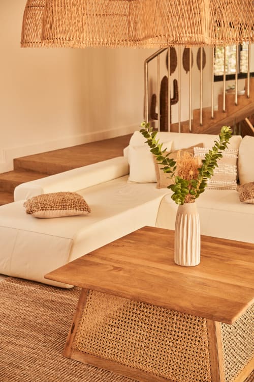 Dormitorio de villa estilo Ibiza en La Maison D'ambrine con sofá crema, muebles de madera, lámpara colgante trenzada y plantas frescas