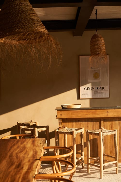 Terraza soleada con lámparas colgantes tejidas, taburetes de madera y póster de Gin & Tonic en la villa La Maison D'ambrine en Chamaret
