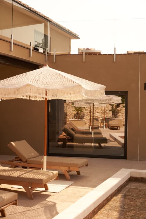 Terraza soleada de la villa La Maison D'ambrine con sombrillas color crema, tumbonas de madera y vista a la piscina en Chamaret