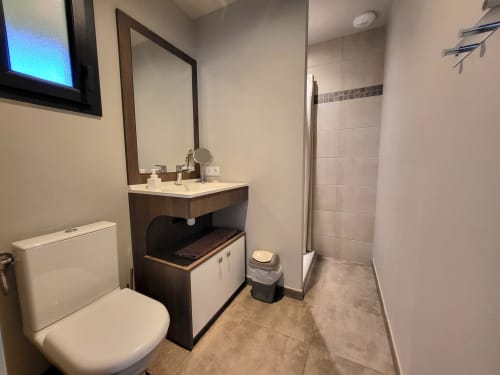 Modernes Badezimmer in der Villa Lantana mit dunklem Waschtisch, Rahmen spiegel, Toilette und gefliester Duschbereich in der Lecci-Wohnung.