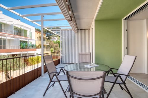 Balcón moderno del hotel Finques Garcia Enrich en Palafrugell con tumbonas, mesa, pared verde y vistas a las colinas