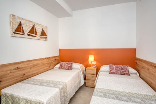 Habitación doble en el hotel Finques Garcia Enrich en Palafrugell con camas de madera, pared acentuada en naranja y decoración náutica con velero
