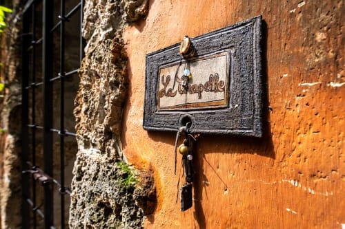 Verwitterte Terrakottamauer mit Holzschild « La Chapelle » und rustikalen Metallschlüsseln darunter im La Bouscatière B&B