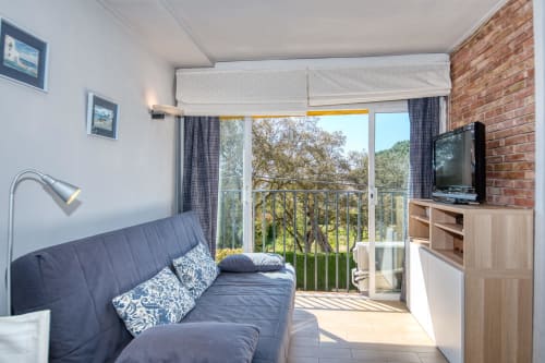 Bright studio apartment in Palafrugell with blue sofa, balcony view of trees, TV, and modern furnishings