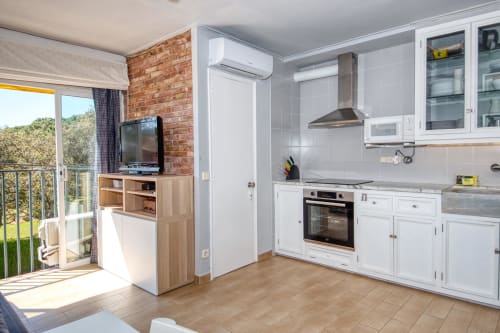 Modern kitchen with white cabinetry, brick accent wall, and balcony view in Palafrugell studio apartment