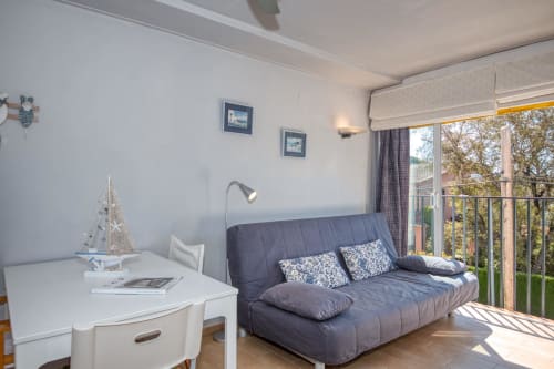 Studio apartment in Palafrugell with dark sofa, white desk, balcony overlooking trees, nautical decor