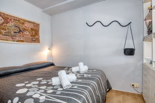 Cozy studio bedroom in Palafrugell with rolled towels, patterned bedspread, wall art, and black shoulder bag on wavy wall