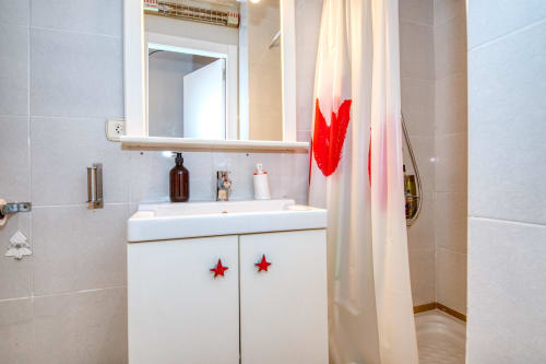 Modern bathroom in Palafrugell apartment with white vanity, red star decorations, and shower with curtain rod.