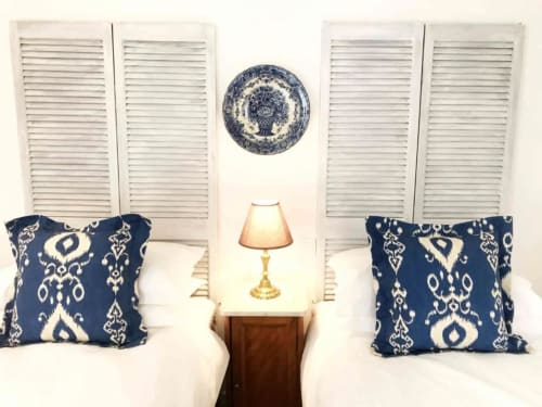 Twin beds with blue damask pillows, white shutters, and bedside lamp in Ciboulette room at Manoir De Rieuzal, LOUBRESSAC