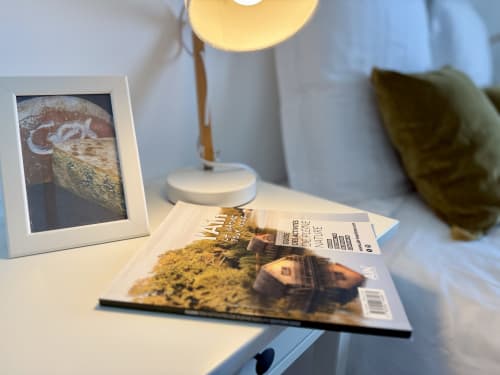 Angolo della camera Gex al Gîte Grange Debout, comodino bianco con lampada, guida alle attività dell’Ain e cornice fotografica.