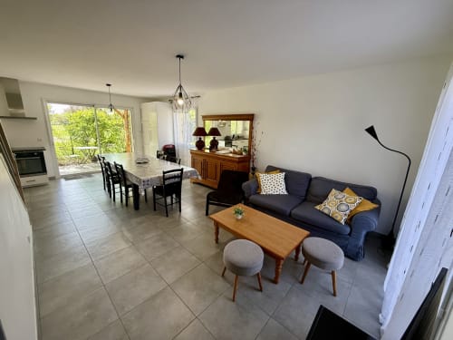 Ampio soggiorno-sala da pranzo al Gîte Grange Debout, con grande tavolo conviviale, divano grigio e vista su terrazza e giardino.