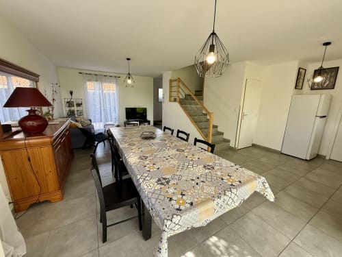 Soggiorno e sala da pranzo luminosi del gîte Grange Debout a Beynost, con ampia tavola conviviale, zona salotto accogliente, scala per il piano superiore e accesso alla terrazza esterna – ideale per una vacanza rilassante vicino a Lione.