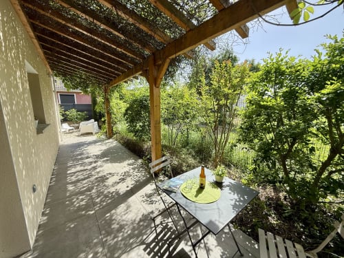 Piccolo tavolo da giardino con bottiglia di birra artigianale sulla terrazza ombreggiata da una pergola vegetale al Gîte Grange Debout.