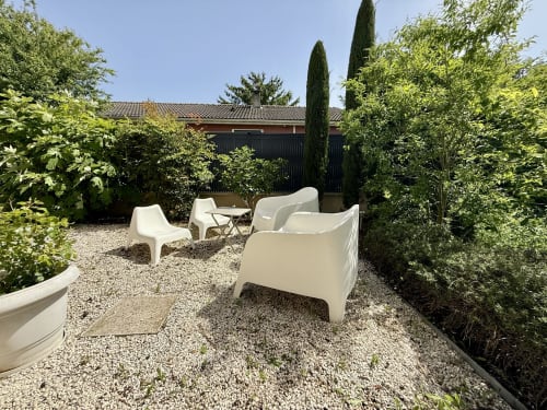 Angolo relax esterno con poltrone bianche moderne posizionate su ghiaia fine, nel giardino intimo del gîte.
