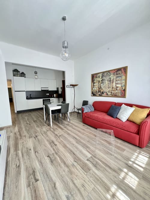 Zona living moderna dell'LA Home Viareggio con divano rosso, cucina a vista, pavimenti in legno e vista città