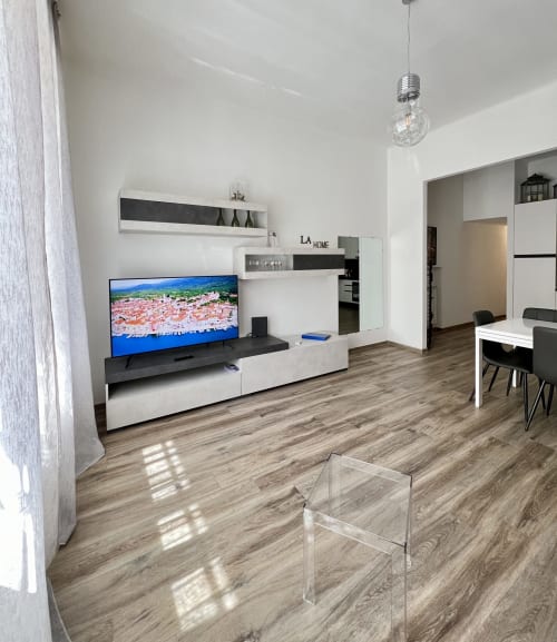 Soggiorno open-space moderno nell'appartamento LA Home di Viareggio, con TV a schermo piatto, scaffalature bianche, pavimento in legno e vista città