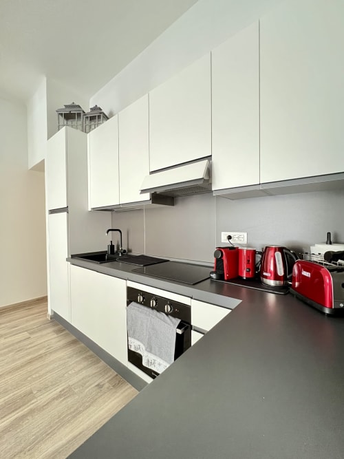 Cucina moderna bianca con piano nero, elettrodomestici rossi e forno incassato dell'appartamento LA Home a Viareggio