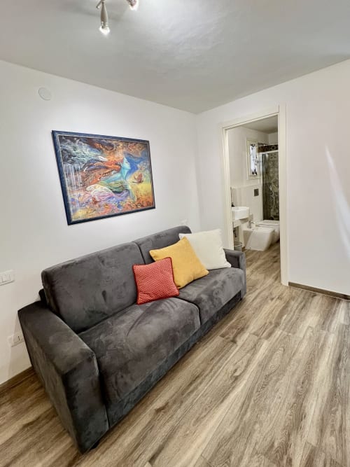 Moderno soggiorno dell'appartamento Puzzle House presso LA Home Viareggio con divano grigio, cuscini colorati e opere d'arte incorniciate