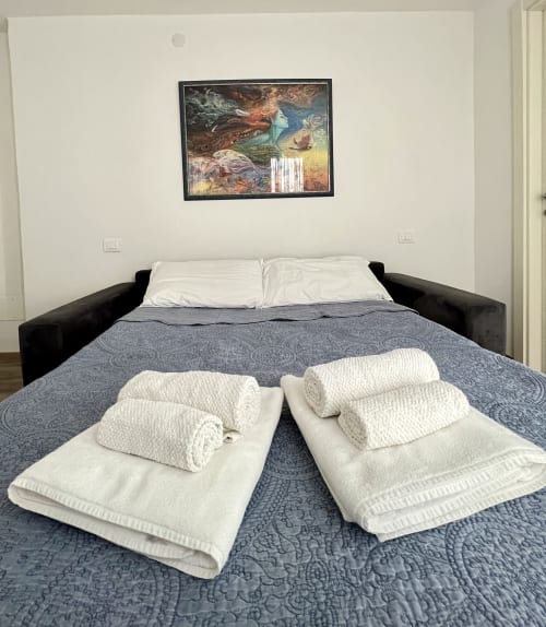 Camera da letto della LA Home Puzzle House a Viareggio con asciugamani arrotolati sul letto, testata nera e quadri incorniciati sopra
