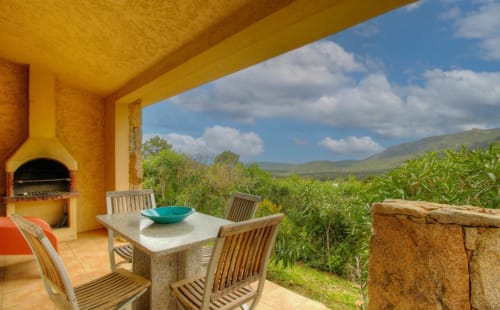 Terrasse Vista D'oro avec table à manger, chaises en bois et foyer en pierre dominant la vallée de Monacia d'Aullène