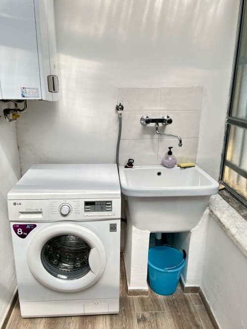 Bagno compatto nell'appartamento LA Home con lavatrice LG bianca, lavabo a muro e secchio d'acqua blu a Viareggio